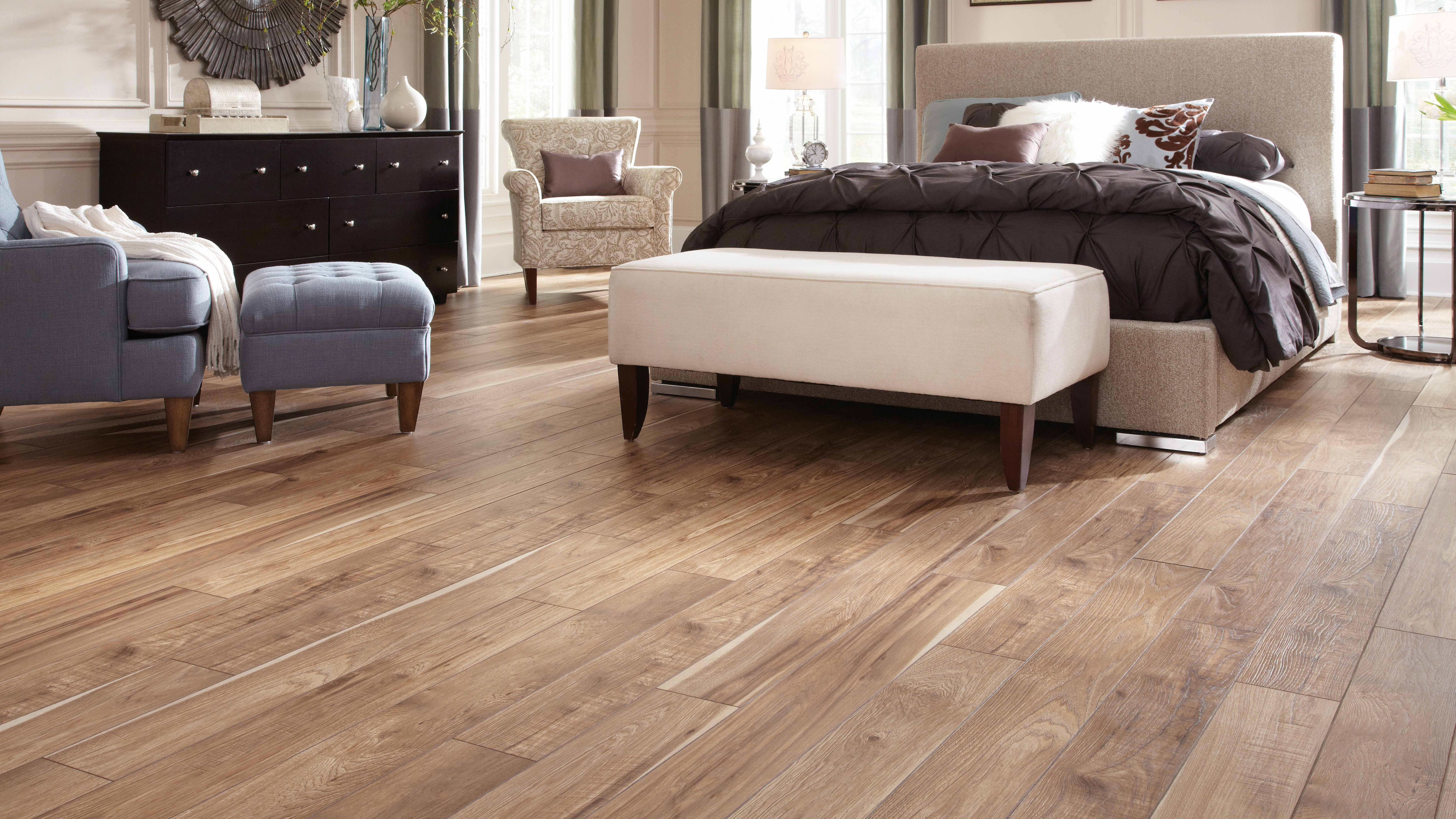 Bedroom scene with laminate wood-look flooring, arm chair, queen sized bed.